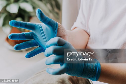 Een Aziatisch Chinees wijfje dat haar latex chirurgische handschoenen thuis vóór het schoonmakensproces draagt Een Aziatisch Chinees wijfje dat haar latex chirurgische handschoenen thuis vóór het schoonmakensproces draagt