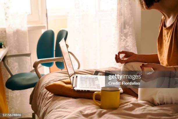 a middle-aged woman in white jeans and a yellow sweater sitting on the bed in a yoga pose in front of a laptop and a cup of coffee - yellow pants stockfoto's en -beelden