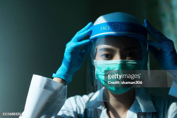 closeup asian female doctor wearing face shield and ppe suit and praying for stop coronavirus outbreak or covid-19, concept of covid-19 quarantine - pandemic illness stock-fotos und bilder