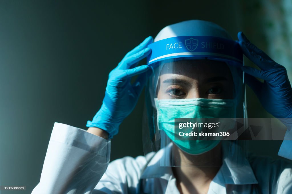 Closeup Asian female Doctor wearing face shield and PPE suit and praying for stop Coronavirus outbreak or Covid-19, Concept of Covid-19 quarantine