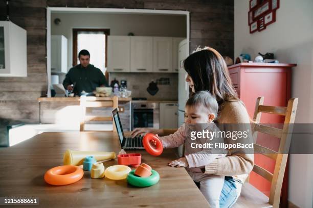 a little girl using a laptop with her mom while the dad is cooking in the kitchen - mother and baby and laptop stock pictures, royalty-free photos & images