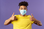 Covid19, healtcare and medicine concept. Enthusiastic happy spanish guy in facial mask, show thumbs-up and smiling with eyes, excited, support social-distancing, prepared for going grocery shopping