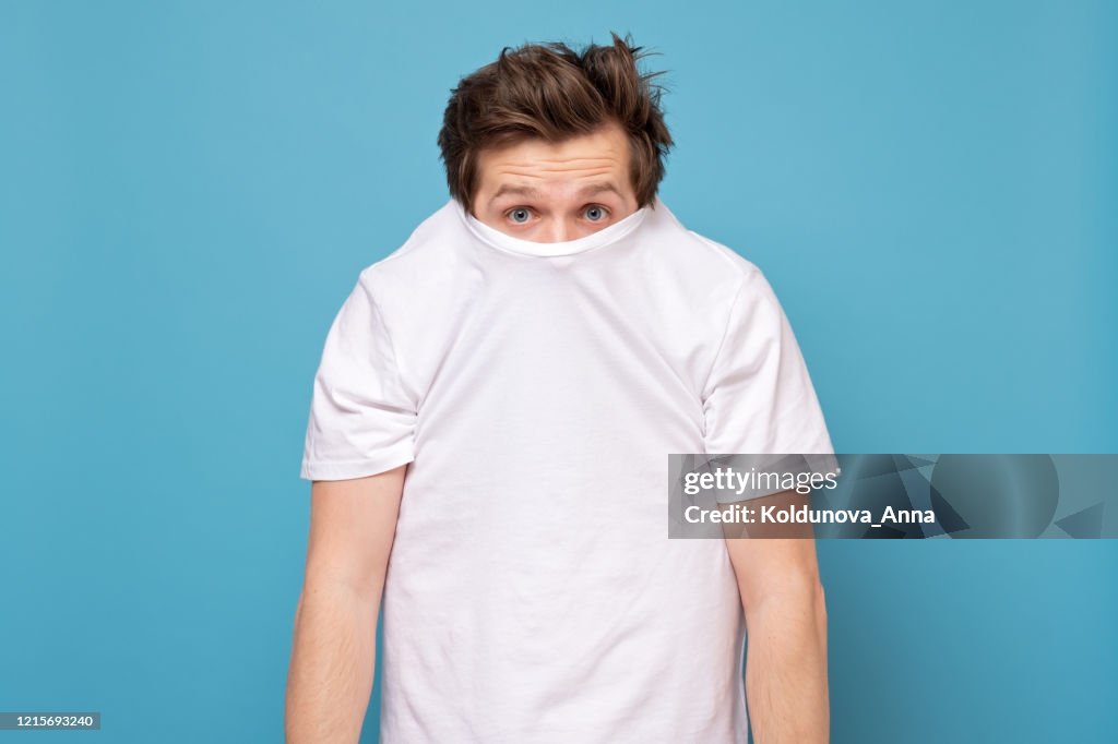 Shy caucasian man hiding behind his white shirt being afraid of coronavirus.