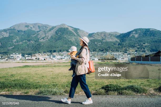 joyful mother and little daughter in the nature walking outdoors on oilseed rape field against blue sunny sky - family hiking in spring outdoors foto e immagini stock