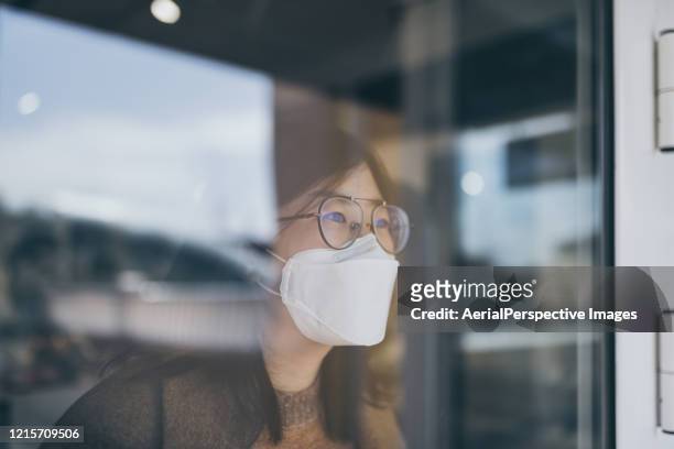 woman looking through window with mask - 風邪マスク ストックフォトと画像