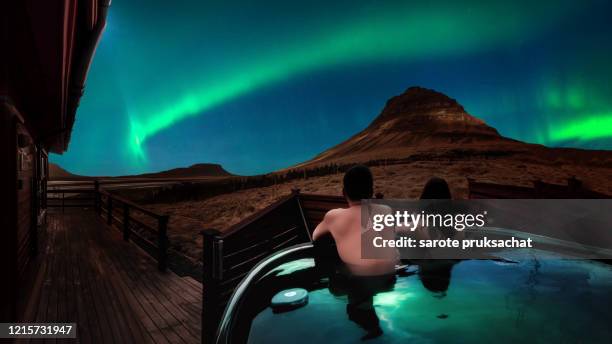 asian couples in a hot tub or onsen of a luxury resort while stunning northern light, aurora borealis at kirkjufell in iceland. - aurora panorama stock pictures, royalty-free photos & images