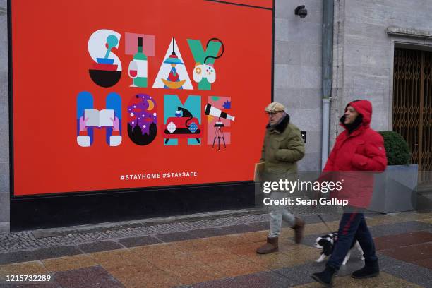 Two men walking a dog who said they did not mind being photographed walk past a creative "Stay Home" billboard hanging on the temporarily shuttered...