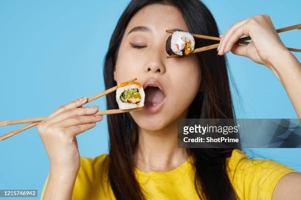 young woman holding sushi rolls in her hands and with closed eyes trying to bite a roll - woman sushi stock-fotos und bilder