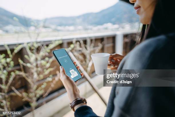 young asian woman using mobile app on smartphone to order food delivery online at home in self isolation during the covid-19 health crisis - politics and government stock pictures, royalty-free photos & images