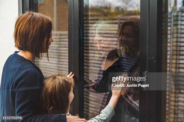 senior lady speaking to daughter and granddaughter through window - quarantaine stockfoto's en -beelden