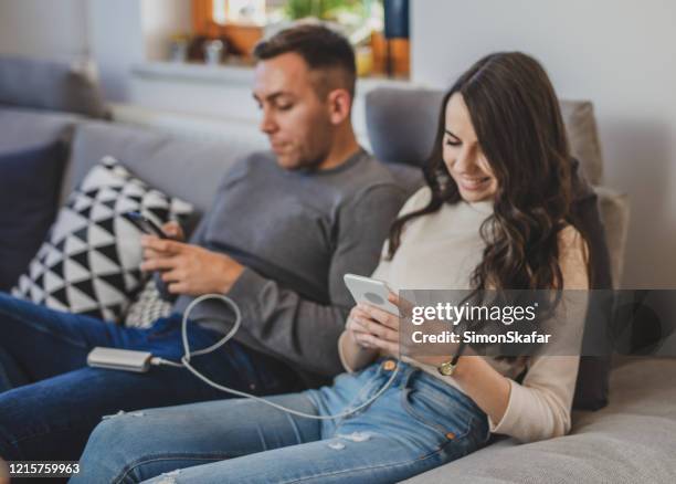 couple using smart phones with power bank on sofa - loader reading stock pictures, royalty-free photos & images