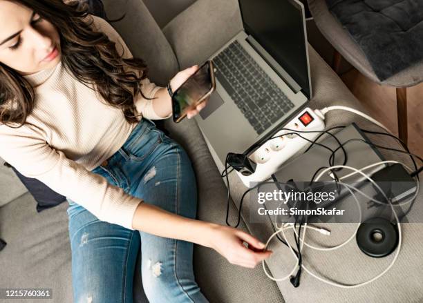 giovane donna carica dispositivi tecnologici sul divano - computer cable foto e immagini stock
