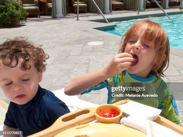 little girl and little boy outside at a hotel pool eating lunch in swim tops in the sunshine. - freibad stock-fotos und bilder