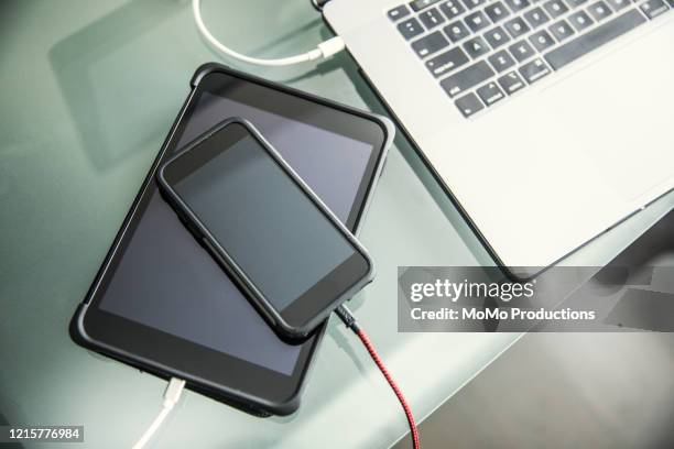 mobile devices and laptop charging on office desk - phone charging stock-fotos und bilder