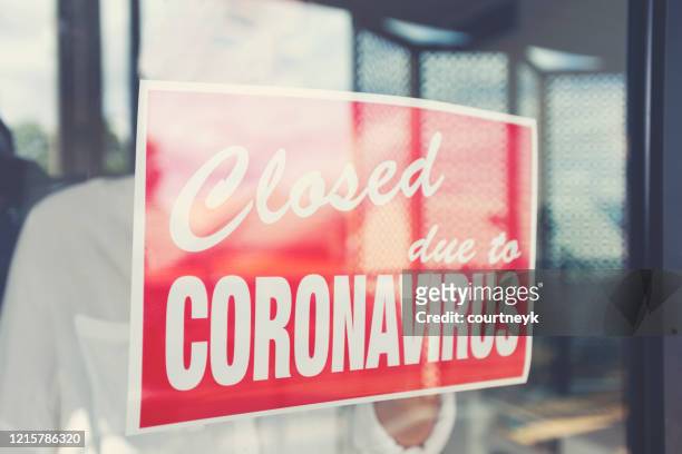 store owner putting up a closed sign in the window - covid-19 economy stock pictures, royalty-free photos & images