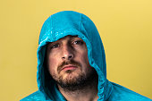 Portrait of a sad man with unshaven face dressed in blue hoodie. Yellow background. Close-up.