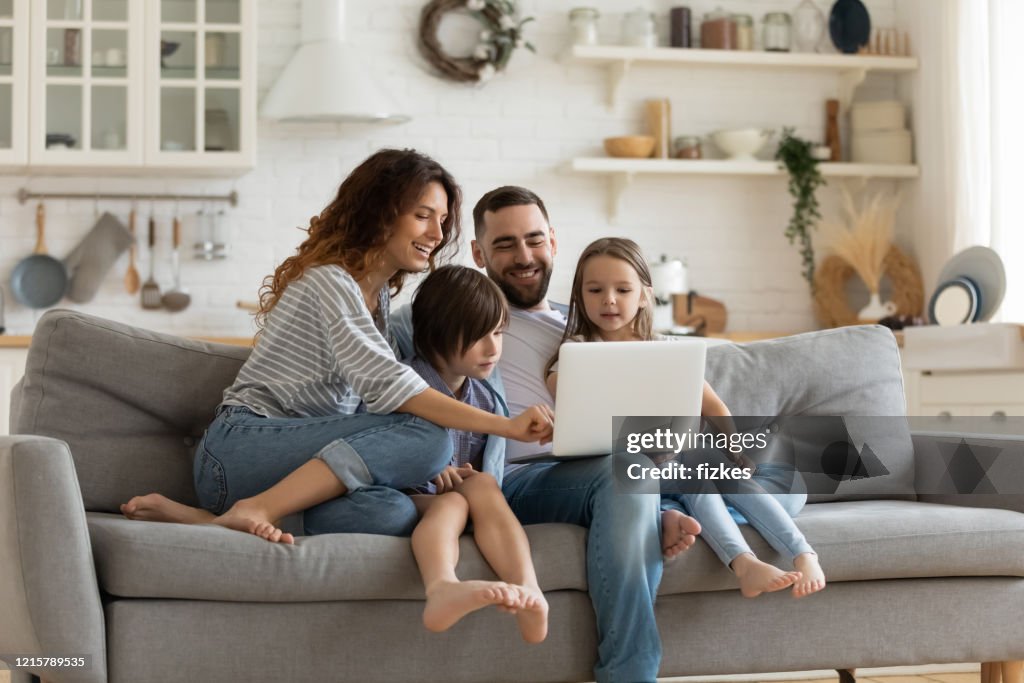 Happy family with kids sit on couch using laptop