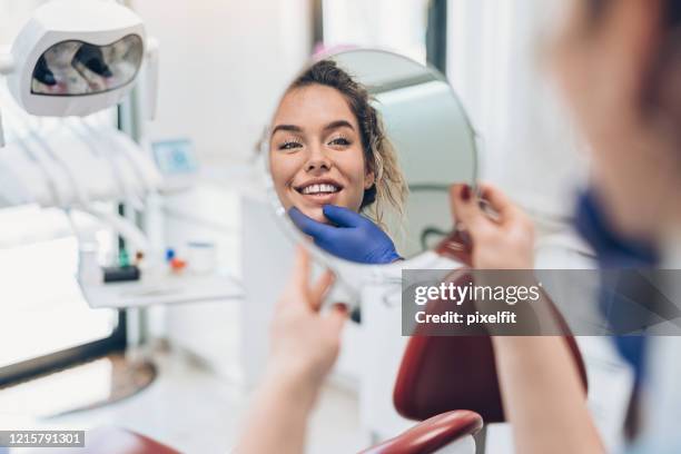 smiling young woman looking in the mirror in the dentist's office - missing teeth stock pictures, royalty-free photos & images