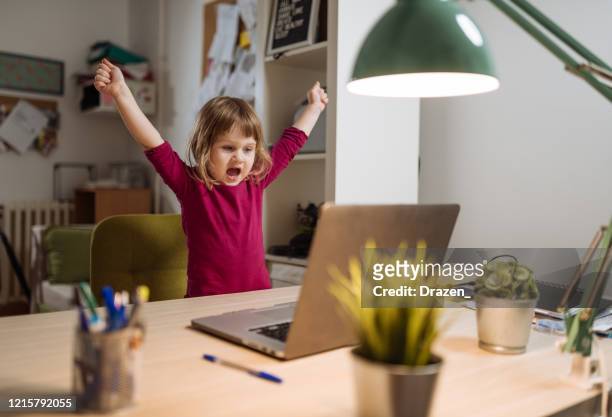 ekstatische dreijährige mädchen feiert den sieg auf videospiel auf laptop - kinder lernen spaß stock-fotos und bilder