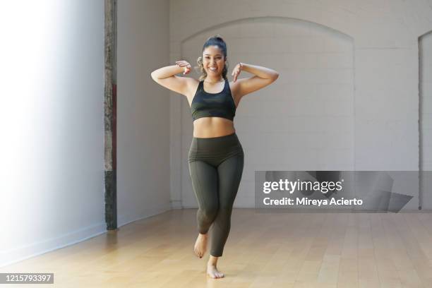 a latinx millennial woman smiles while rehearsing in a dance studio wearing olive green and camouflage sportswear. - legging stock-fotos und bilder