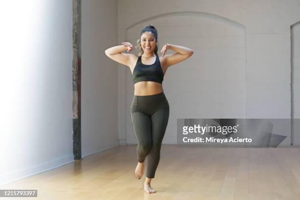 a latinx millennial woman smiles while rehearsing in a dance studio wearing olive green and camouflage sportswear. - leggings imagens e fotografias de stock