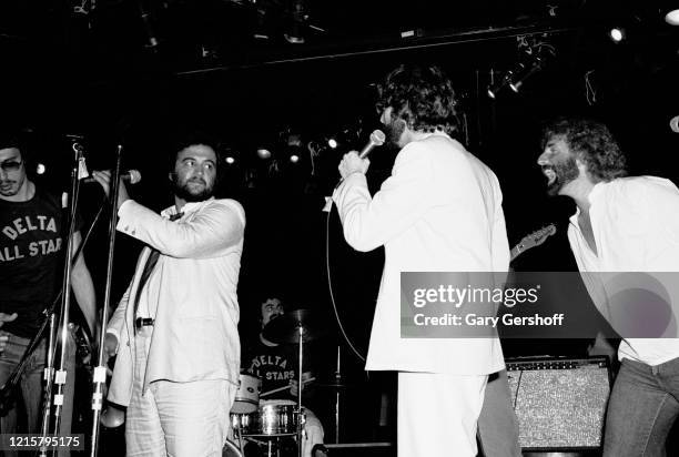 View of, from left, American actor & comedian John Belushi and musicians Stephen Bishop and Andrew Gold as they perform onstage at Greenwich...