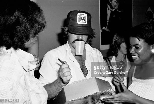 American actor Bruce McGill holds a plastic cup in his mouth as he signs autographs for fans at Greenwich Village's Village Gate nightclub, New York,...