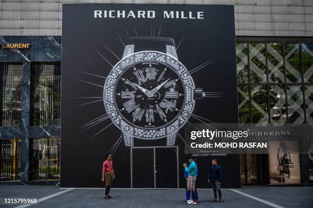 Men wearing traditional Baju Melayu clothes take pictures next to a large watch advertising billboard outside a shopping mall in Kuala Lumpur on May...