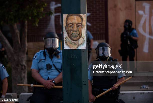 Portrait of George Floyd hangs on a street light pole as police officers stand guard at the Third Police Precinct during a face off with a group of...