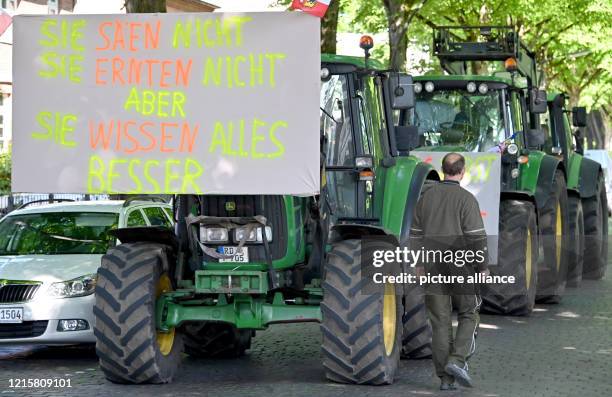 May 2020, Schleswig-Holstein, Neumünster: Protesting farmers stand with tractors in front of the regional office of the nature conservation...