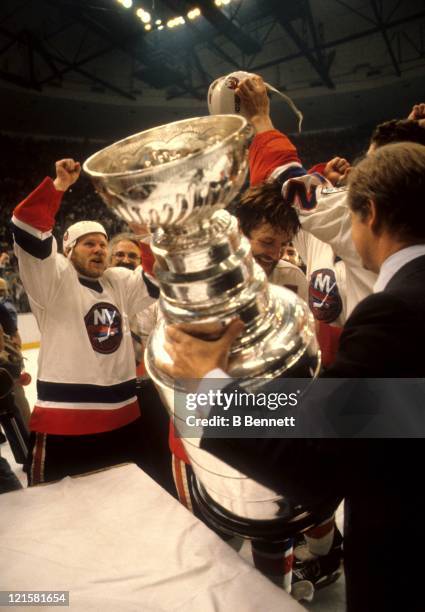 John Ziegler, president of the NHL, awards the Stanley Cup Trophy to Denis Potvin of the New York Islanders as teammate Butch Goring celebrates their...