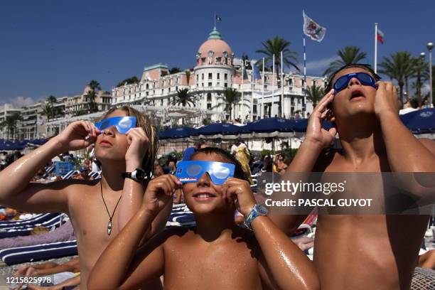 Des enfants observent l'éclipse solaire, le 11 août 1999 devant l'hôtel Negresco sur une plage de Nice, où de nombreux touristes sont venus assister...