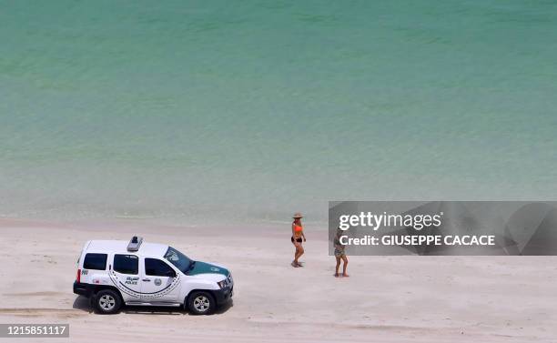 Bathers stare at a police car patroling a public beach at the Jumeirah Beach Residence in the Gulf city of Dubai on May 25, 2020.