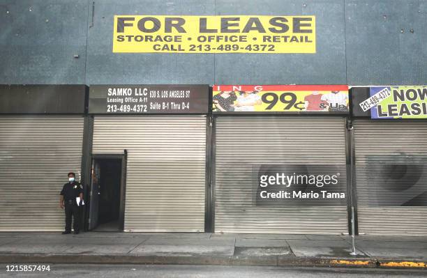 Security guard wears a face mask while standing outside shuttered shops and a 'For Lease' sign amid the global coronavirus pandemic on March 30, 2020...