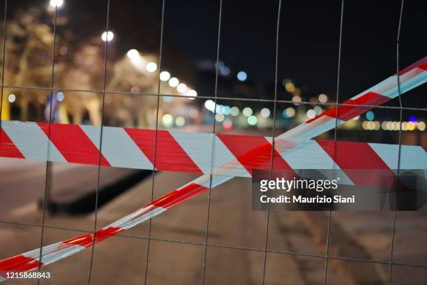 cordon tape by chainlink fence against sky - barrikade stock-fotos und bilder