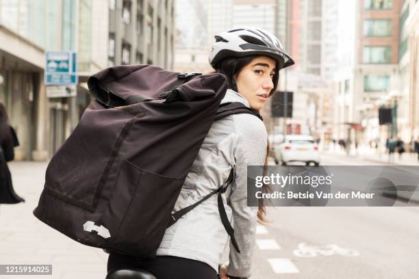 female courier looks over shoulder, while cycling with delivery bag. - looking in bag stock-fotos und bilder