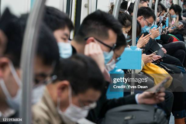Commuters in protective masks look at their smartphones while riding a subway train during evening peak on March 31, 2020 in Shanghai, China. Health...