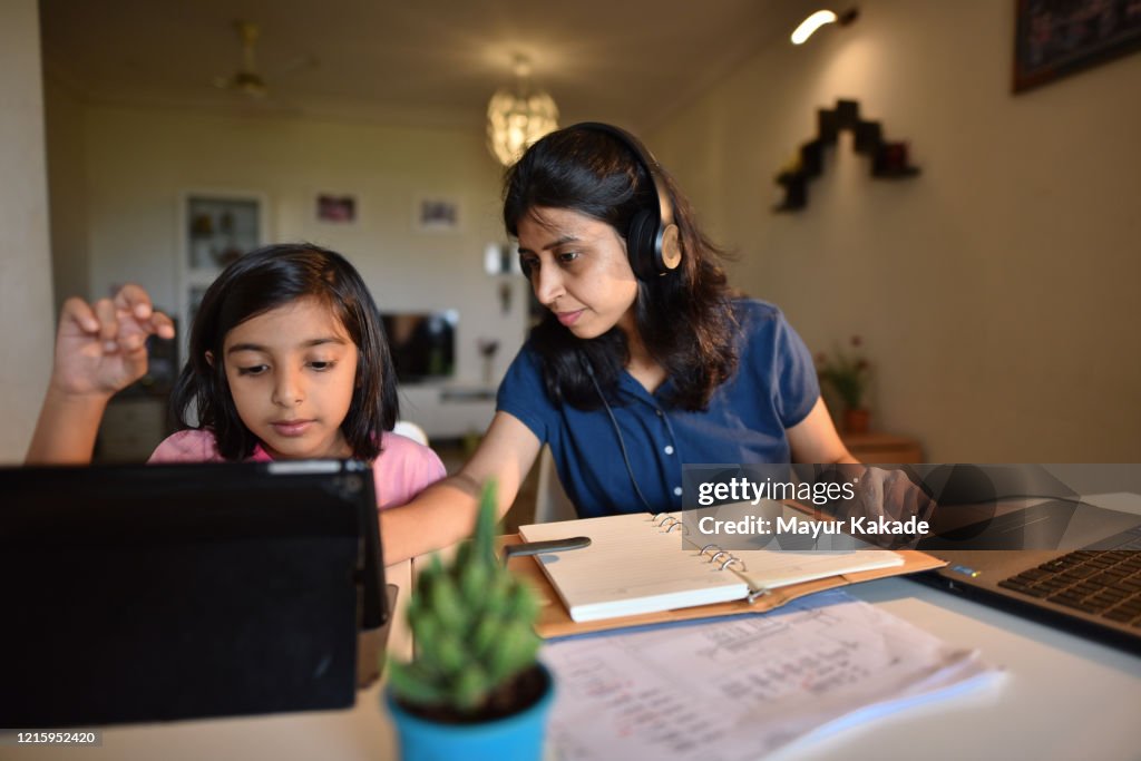 Woman working from home while daughter using digital tablet
