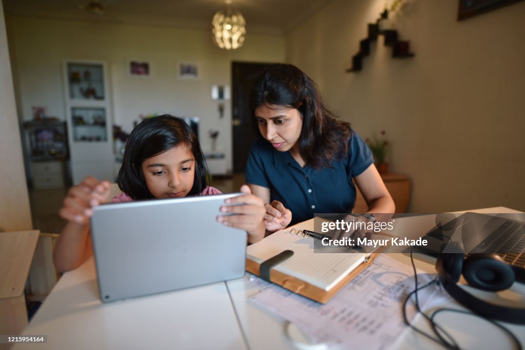 Woman working from home while daughter using digital tablet