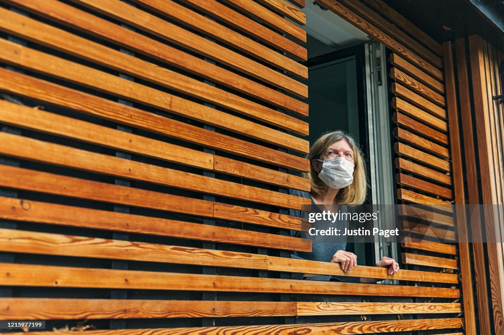 Senior woman with mask looking out of window