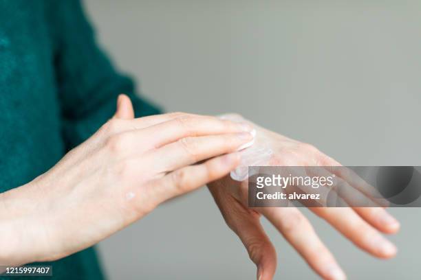 donna che applica crema per le mani per alleviare la pelle secca causata dal disinfettante per le mani - mettersi la crema foto e immagini stock