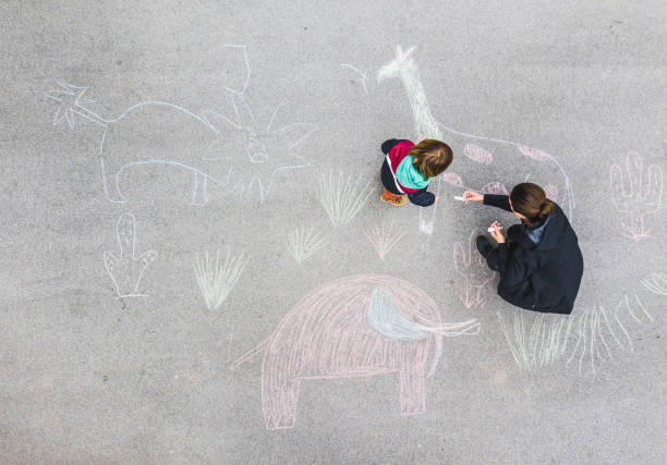 young kid and his mother drawing on asphalt with chalk - zoo art stock pictures, royalty-free photos & images