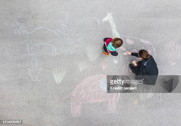 young kid and his mother drawing on asphalt with chalk - sidewalk chalk drawing stock pictures, royalty-free photos & images