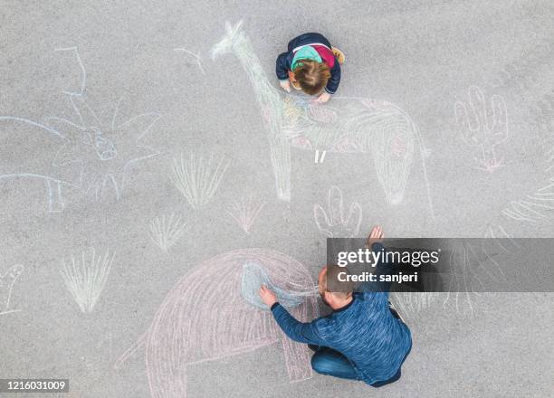young kid and his father drawing on the asphalt with chalk - sidewalk chalk drawing stock pictures, royalty-free photos & images