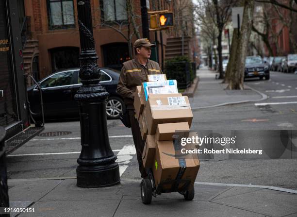 Delivery man for United Parcel Service, UPS, moves his hand truck loaded with packages through a residential neighborhood in Brooklyn, New York on...