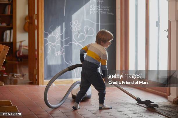 young helpful boy with vacum cleaner vacums the kitchen tiled floor - domestic chores stock pictures, royalty-free photos & images