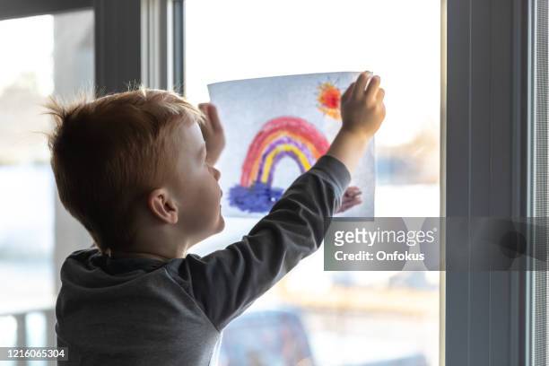 jeune garçon collant son dessin sur la fenêtre de la maison pendant la crise de covid-19 - pandemic illness photos et images de collection