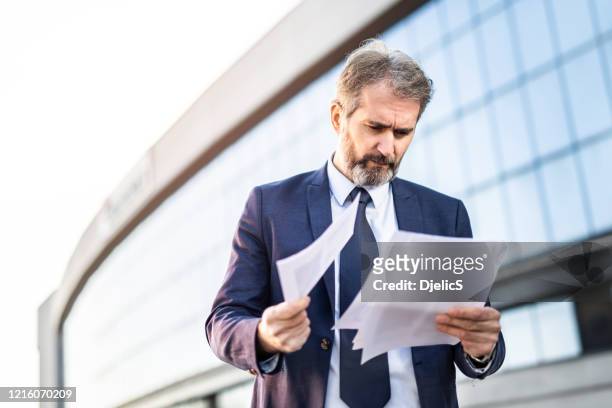seriöser geschäftsmann, der sich die papiere vor einem bürogebäude anschaut. - rejection stock-fotos und bilder