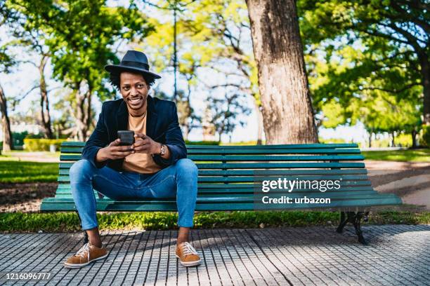 smiling man with phone on bench - bench stock pictures, royalty-free photos & images