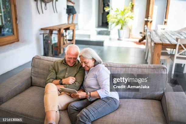 senior paar sitzen zusammen auf sofa mit digitalen tablet - couple tablet house stock-fotos und bilder